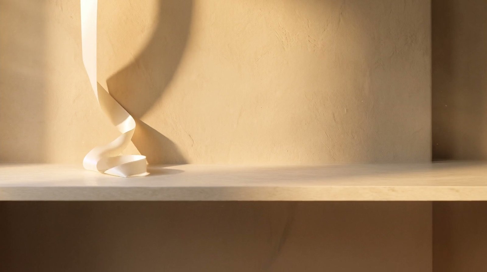 A length of ivory silk settled into a soft coil on a pale limestone ledge, in warm afternoon light.